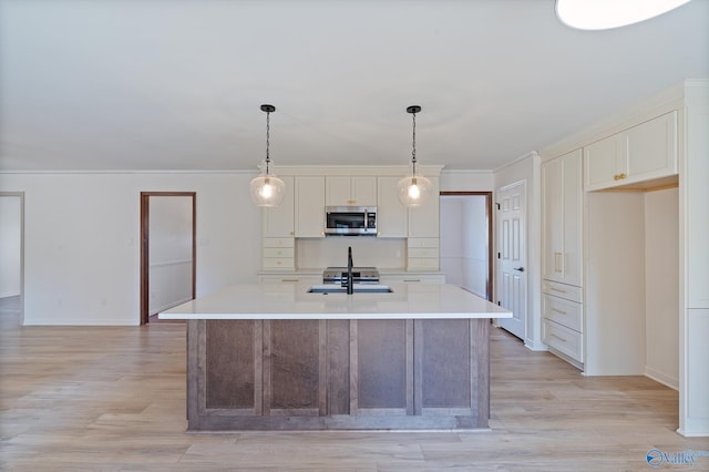 kitchen with ornamental molding, decorative light fixtures, a center island with sink, and light wood-type flooring