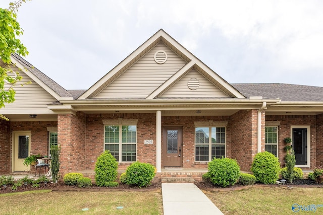 view of front of home featuring covered porch, brick siding, a front yard, and roof with shingles