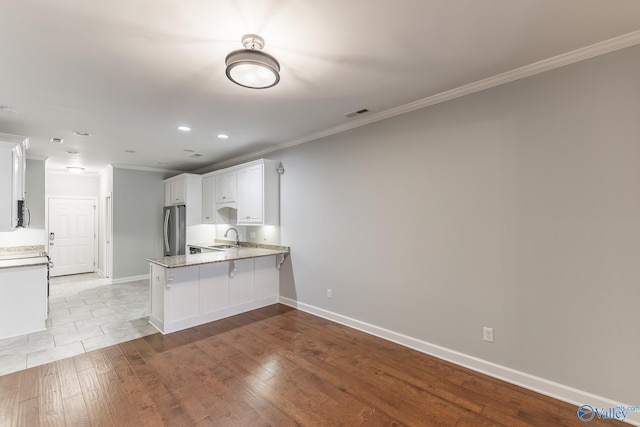 kitchen with crown molding, freestanding refrigerator, a peninsula, white cabinetry, and a sink