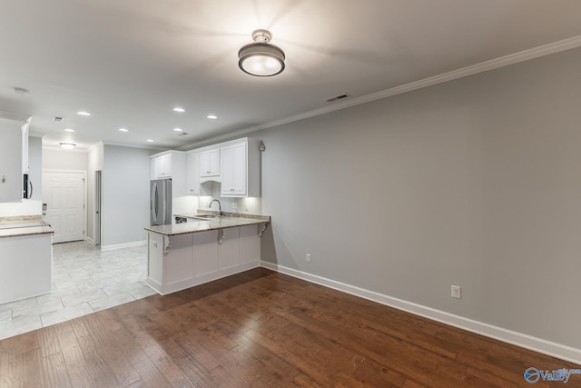 kitchen with crown molding, a peninsula, white cabinets, a sink, and stainless steel appliances