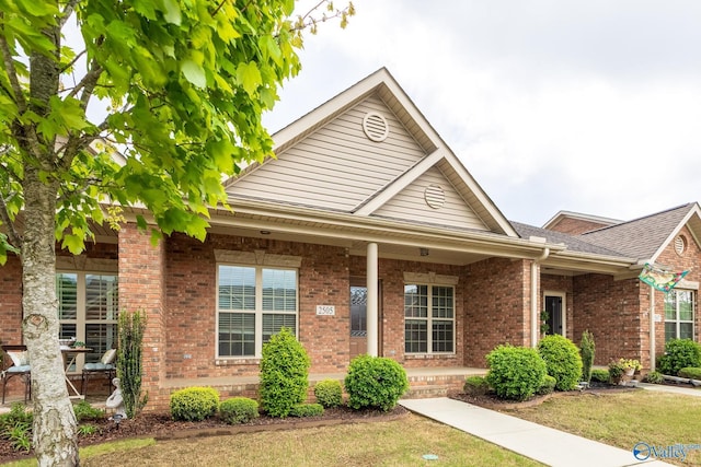 view of front of house featuring covered porch, a shingled roof, a front lawn, and brick siding
