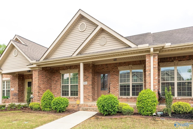 view of front of home with covered porch, brick siding, and a shingled roof