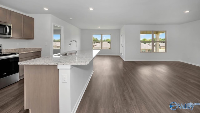 kitchen with sink, a kitchen island with sink, stainless steel appliances, light stone countertops, and dark hardwood / wood-style flooring