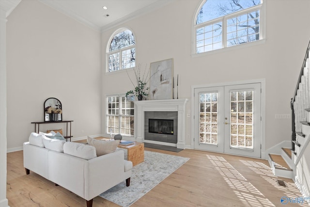 living room featuring french doors, a towering ceiling, crown molding, a tile fireplace, and light hardwood / wood-style floors