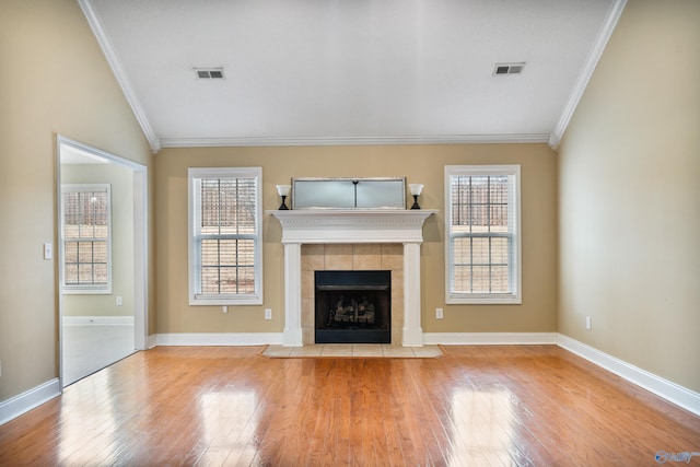 unfurnished living room with crown molding, lofted ceiling, a tiled fireplace, and light wood-type flooring