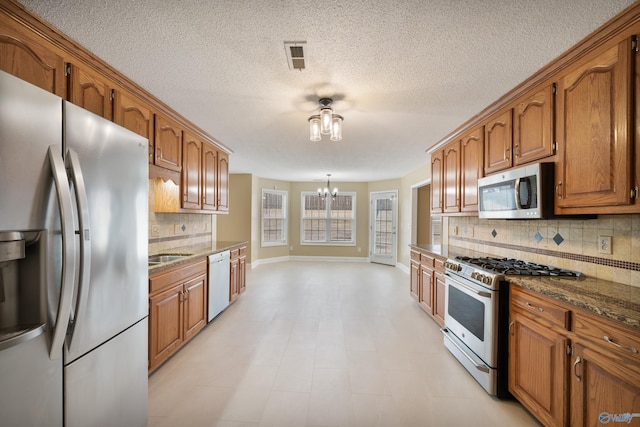 kitchen featuring dark stone countertops, a notable chandelier, appliances with stainless steel finishes, and backsplash