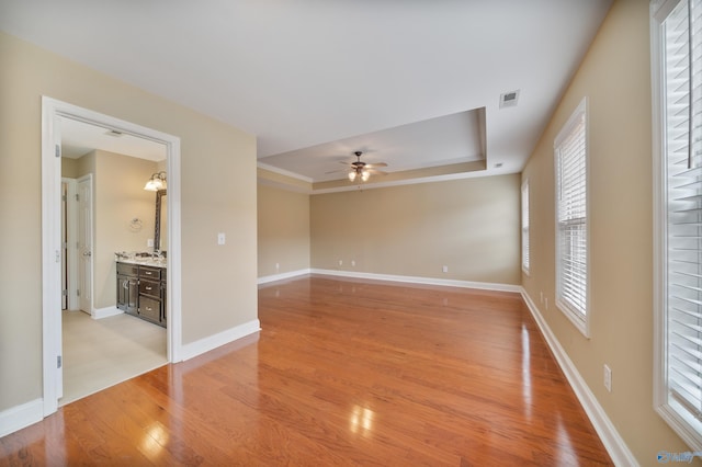 unfurnished room featuring ceiling fan, a raised ceiling, and light hardwood / wood-style flooring