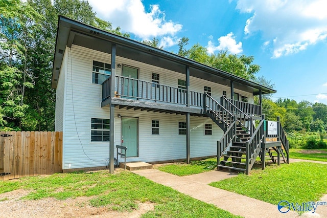 view of front of property featuring covered porch, stairs, fence, and a front lawn