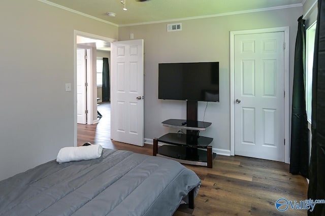 bedroom with baseboards, crown molding, visible vents, and wood finished floors