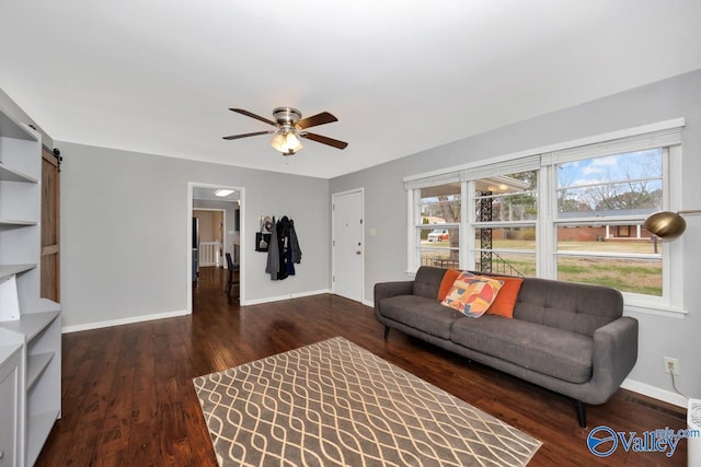 living area featuring a barn door, wood finished floors, baseboards, and ceiling fan