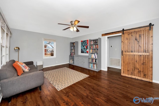 living area with visible vents, wood finished floors, a barn door, baseboards, and ceiling fan