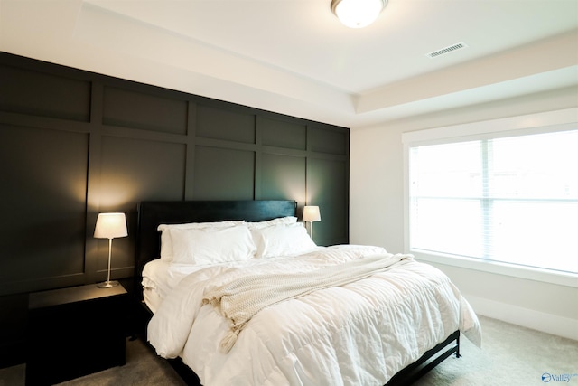 carpeted bedroom with a raised ceiling and multiple windows