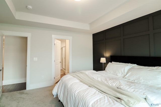 carpeted bedroom featuring a raised ceiling and connected bathroom