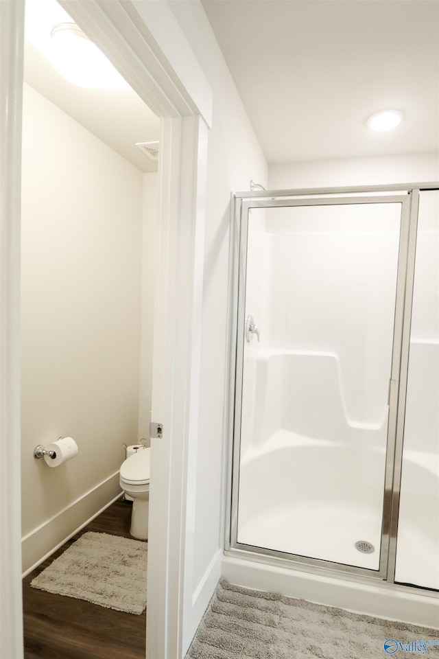 bathroom with hardwood / wood-style floors, a shower with shower door, and toilet