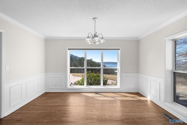 unfurnished dining area featuring dark wood-style flooring, wainscoting, a textured ceiling, and an inviting chandelier