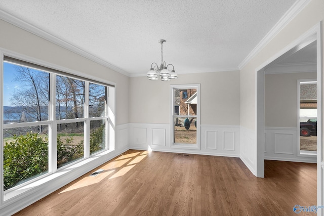 unfurnished dining area with a chandelier, visible vents, a textured ceiling, and wood finished floors