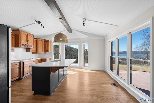 kitchen featuring brown cabinetry, a water view, a kitchen island with sink, light countertops, and pendant lighting