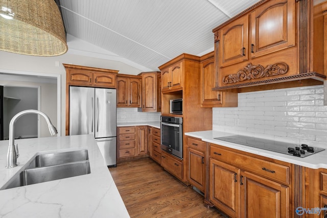 kitchen featuring stainless steel appliances, dark wood-style flooring, a sink, vaulted ceiling, and brown cabinetry