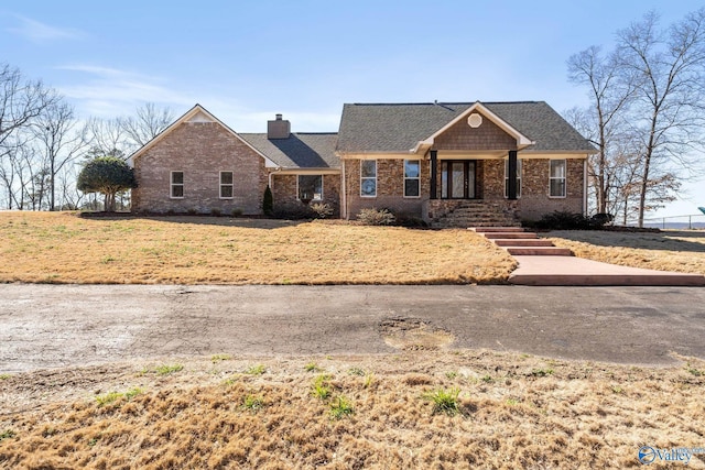 view of front of house featuring roof with shingles, a chimney, and brick siding