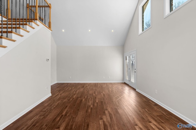 unfurnished living room featuring a healthy amount of sunlight, dark wood finished floors, stairway, and a high ceiling
