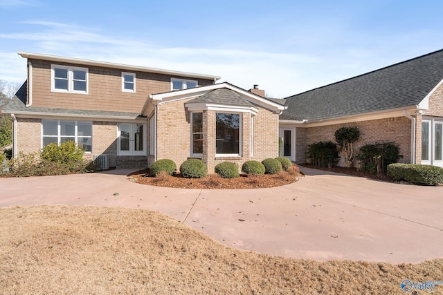 traditional-style house featuring a chimney, central AC, concrete driveway, and brick siding