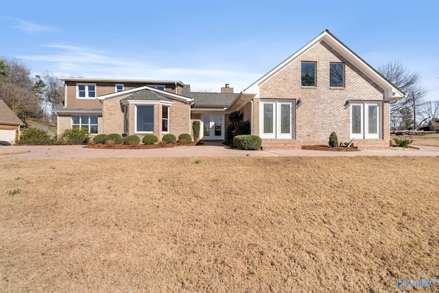 traditional home featuring a front yard, a chimney, and brick siding