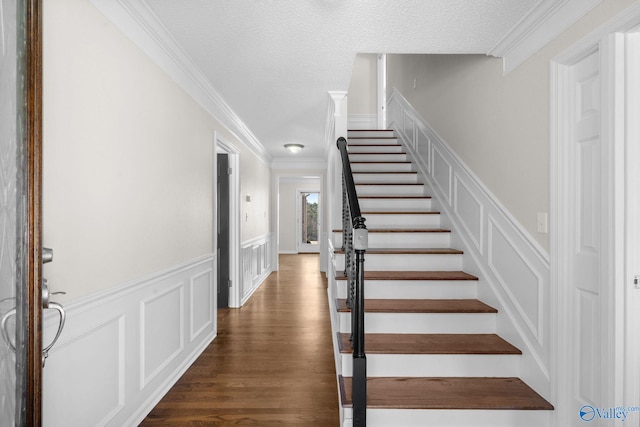 stairs with a wainscoted wall, crown molding, a decorative wall, a textured ceiling, and wood finished floors
