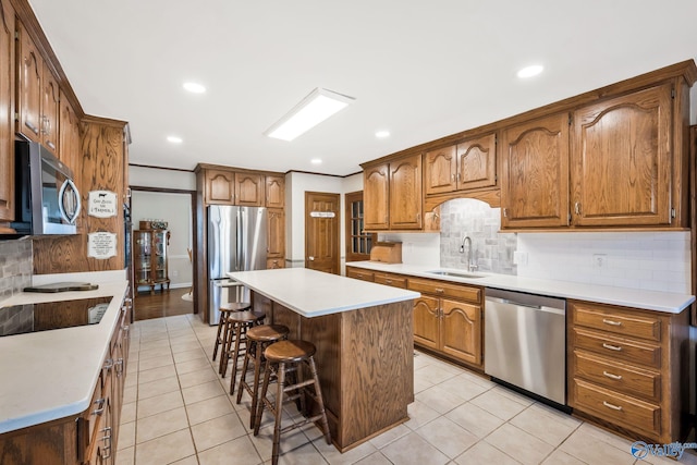 kitchen with brown cabinets, stainless steel appliances, light countertops, a sink, and a kitchen breakfast bar