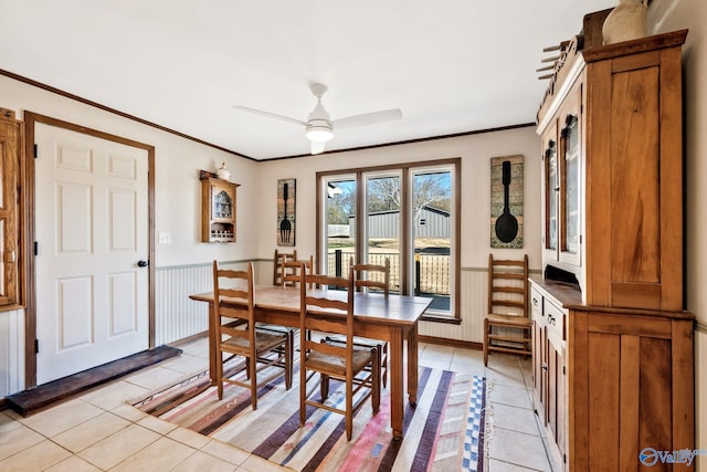 dining room with light tile patterned floors, crown molding, a ceiling fan, and a wainscoted wall