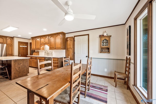 dining space featuring light tile patterned flooring, a wainscoted wall, a ceiling fan, baseboards, and ornamental molding