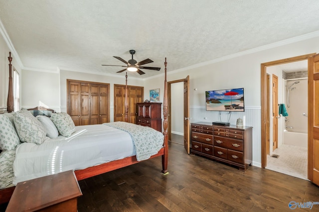 bedroom with dark wood-style flooring, wainscoting, a textured ceiling, and two closets