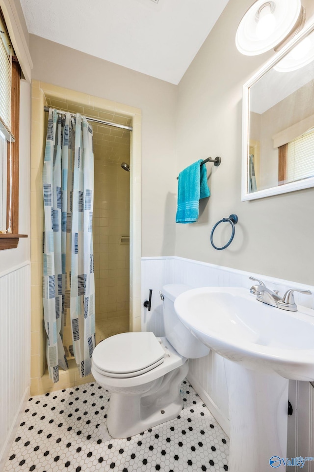 full bath featuring a stall shower, tile patterned flooring, wainscoting, and toilet