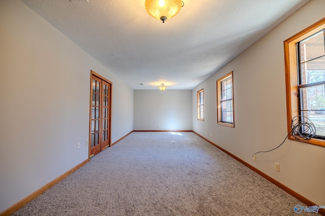 empty room with carpet flooring, a healthy amount of sunlight, a textured ceiling, and baseboards