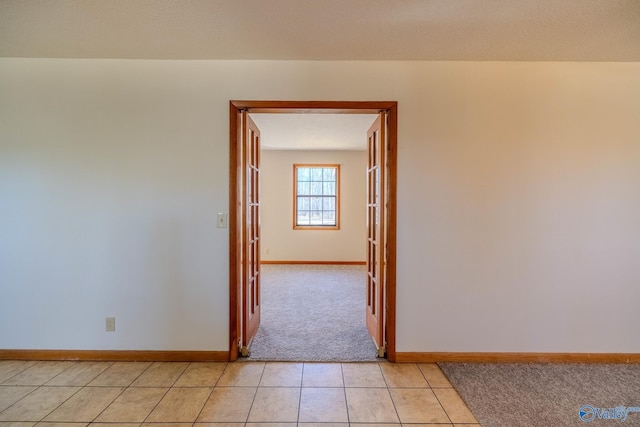 spare room featuring light tile patterned floors, baseboards, and light colored carpet