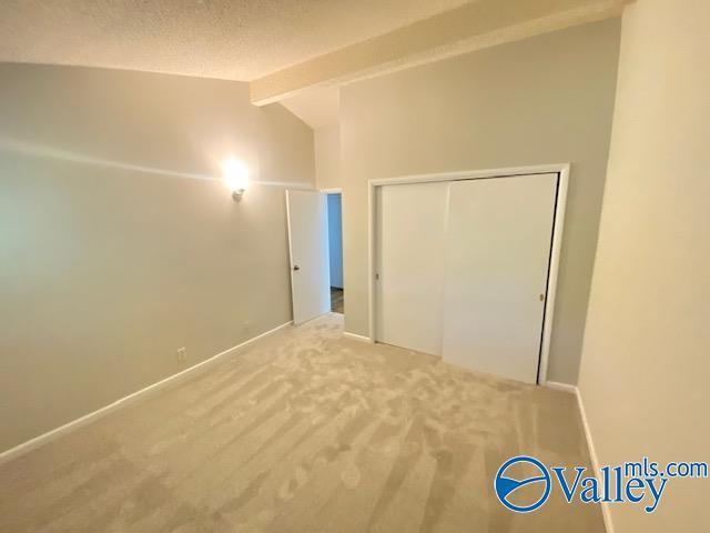 unfurnished bedroom featuring carpet floors, a closet, and vaulted ceiling with beams