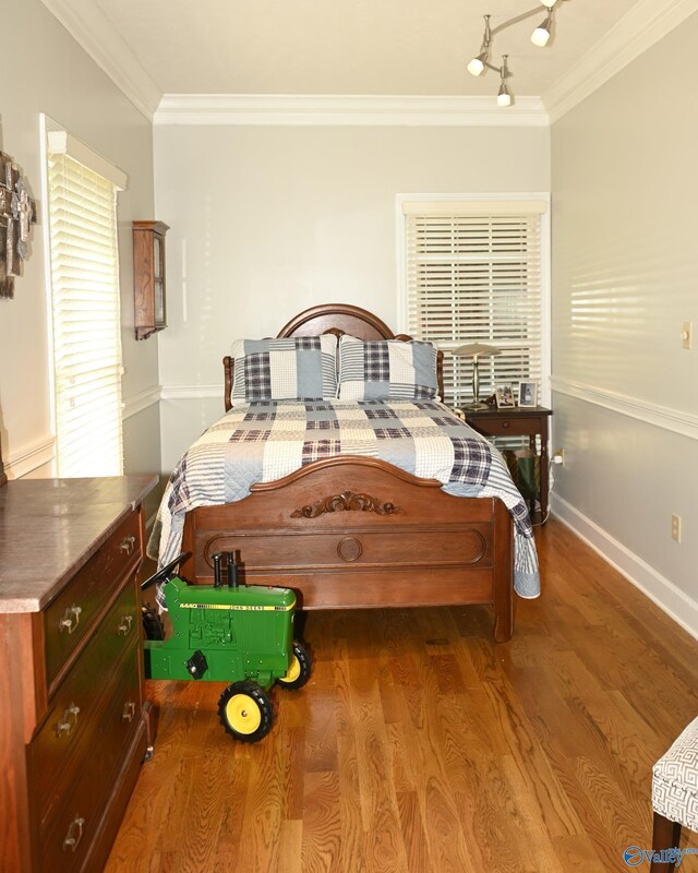 bedroom with hardwood / wood-style flooring, track lighting, and ornamental molding