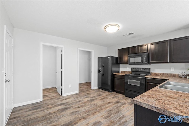 kitchen with light wood-type flooring, a textured ceiling, dark brown cabinetry, sink, and black appliances