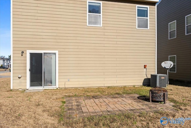 rear view of property featuring a lawn, a fire pit, a patio area, and central air condition unit