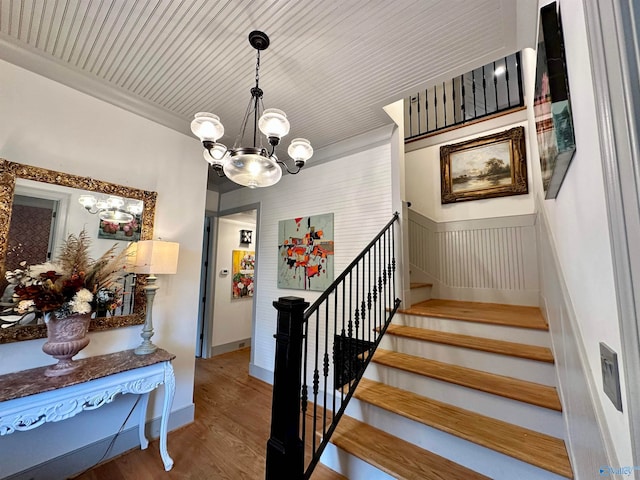 stairs featuring ornamental molding, wood-type flooring, and a chandelier