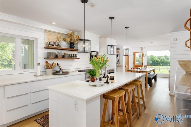 kitchen with white cabinetry, decorative light fixtures, a center island, and light hardwood / wood-style floors