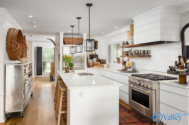 kitchen with sink, white cabinetry, stainless steel range, pendant lighting, and a kitchen island with sink