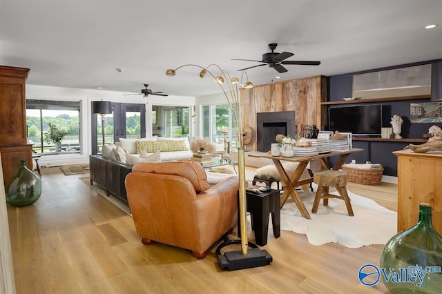 living room featuring ceiling fan, a large fireplace, and light wood-type flooring