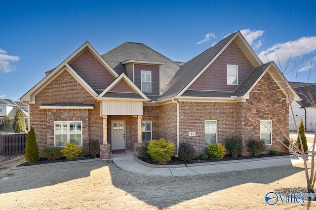 craftsman inspired home featuring stone siding, roof with shingles, fence, and brick siding