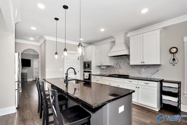 kitchen featuring arched walkways, premium range hood, a sink, appliances with stainless steel finishes, and dark wood finished floors