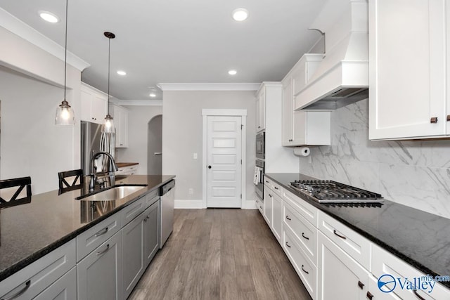 kitchen featuring arched walkways, stainless steel appliances, tasteful backsplash, a sink, and premium range hood