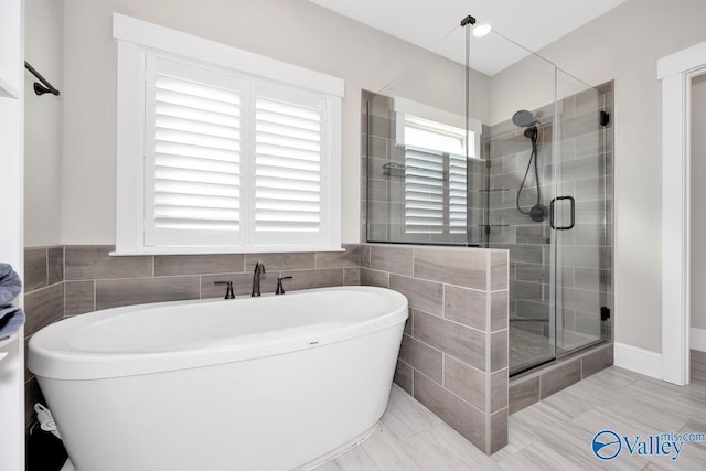 full bath featuring a stall shower, a freestanding bath, and tile walls