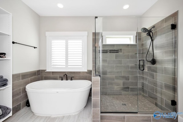 full bathroom with a stall shower, a soaking tub, a wainscoted wall, and tile walls