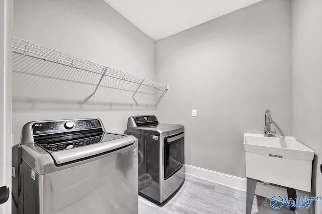 laundry area with laundry area, a sink, independent washer and dryer, and baseboards