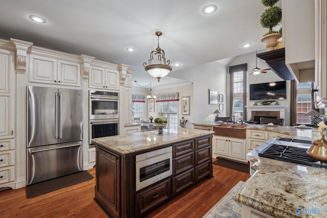 kitchen with a fireplace, appliances with stainless steel finishes, dark wood-type flooring, dark brown cabinets, and light stone countertops