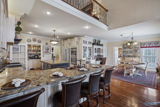 kitchen featuring light stone counters, stainless steel double oven, a sink, dark wood finished floors, and crown molding